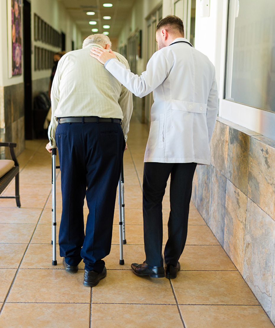 a doctor helping an elderly patient walk down a hallway