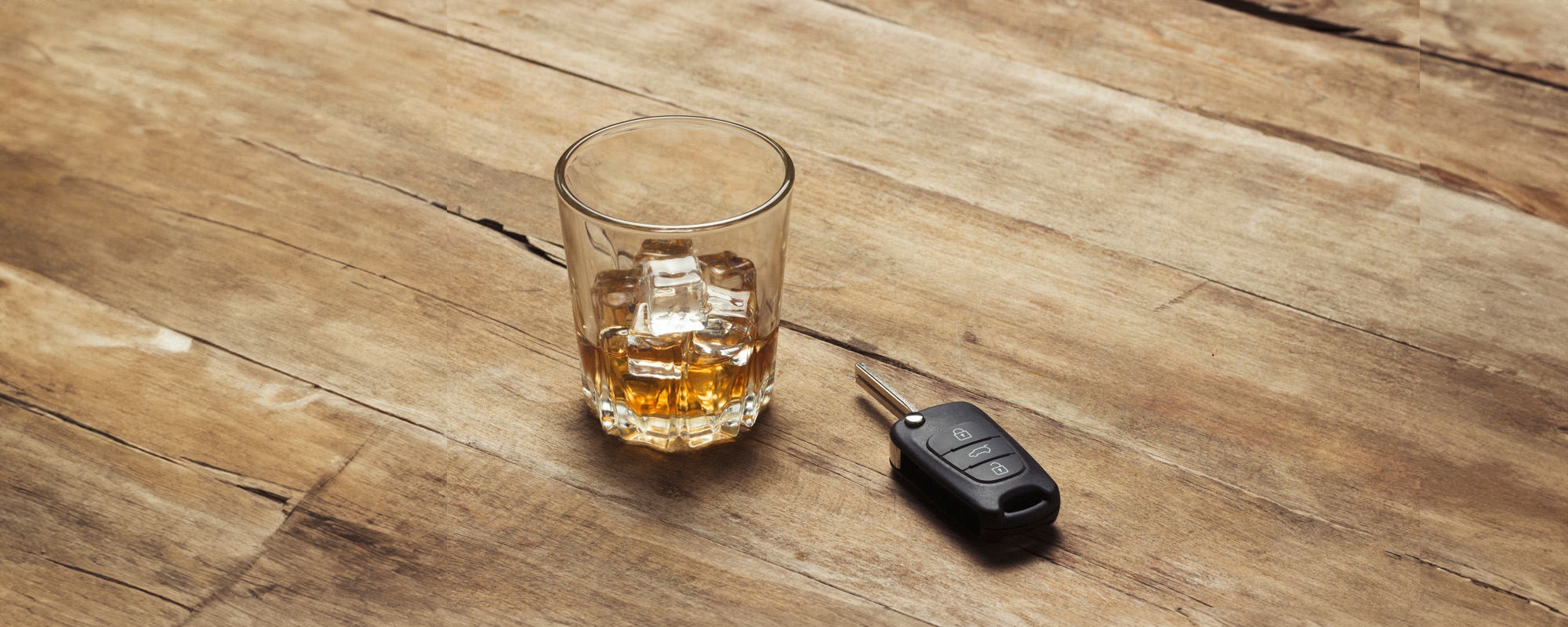 glass with whiskey and ice and car keys on a wooden background